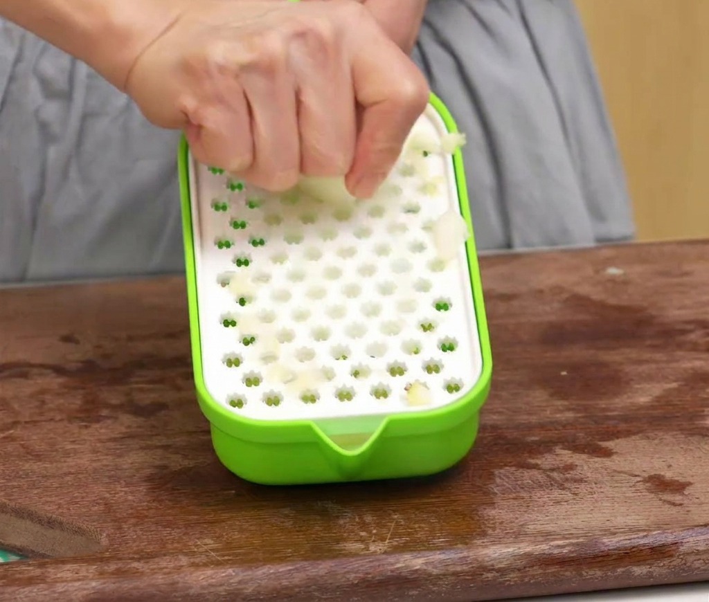 Une personne utilise une râpe en plastique pour transformer une pomme épluchée en pulpe sur une planche en bois.