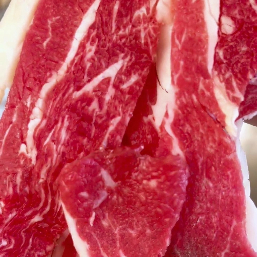 Vue rapprochée de tranches de bœuf frais et marbré empilées dans un grand bol en acier inoxydable.