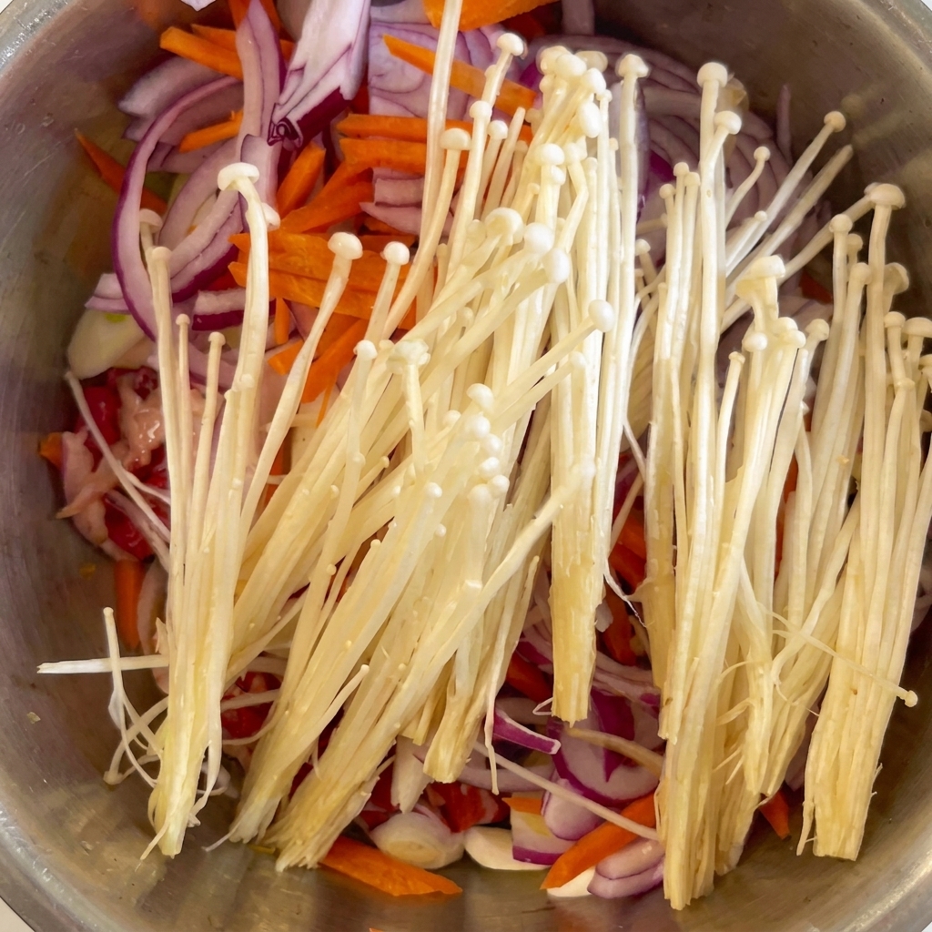 Champignons enoki blancs frais et gousses dail hachées placés sur le bœuf, les oignons et les carottes.