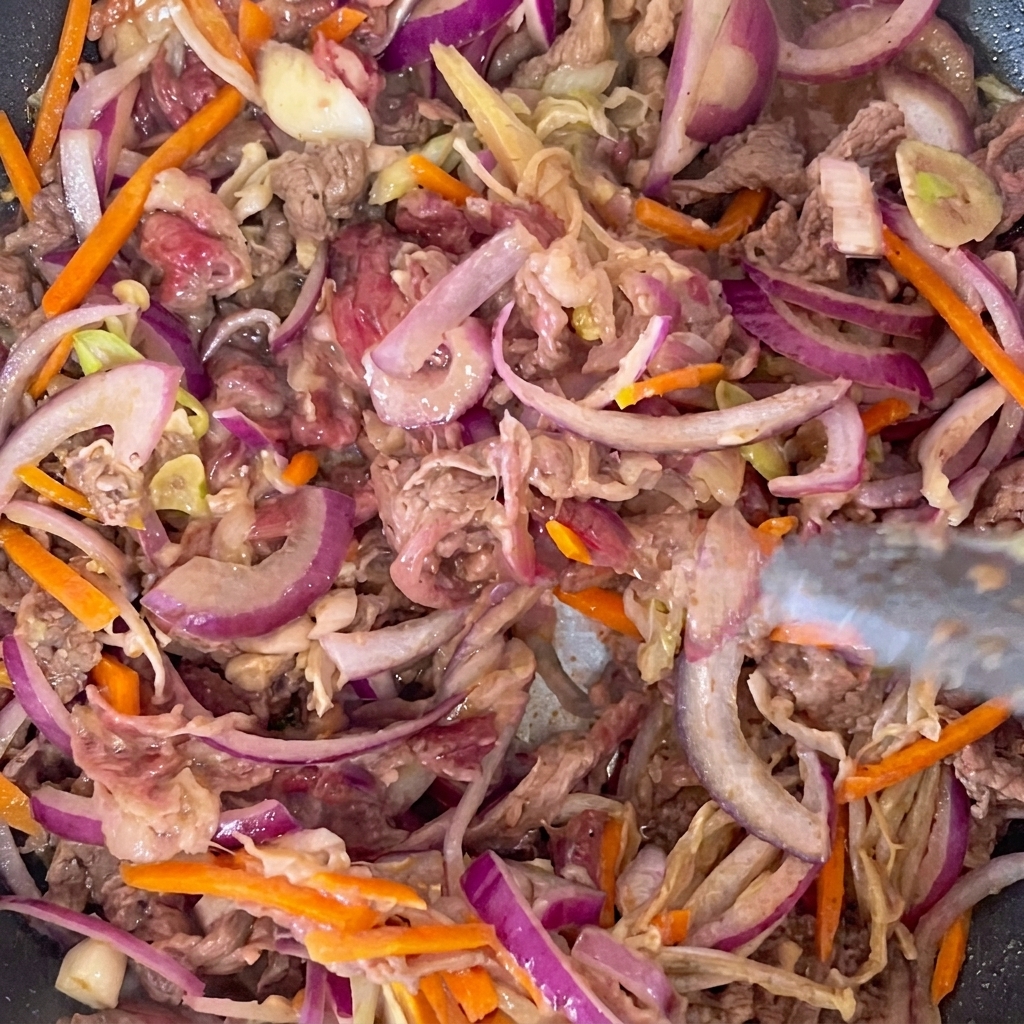 Lamelles de bœuf mariné et légumes assortis cuisant dans une poêle chaude.
