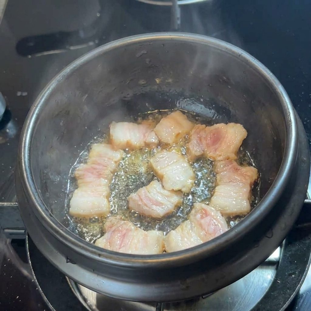 Tranches de poitrine de porc grillant dans leur gras au fond dun pot en pierre noir.