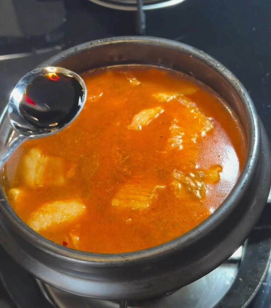 Une cuillère en argent versant de la sauce soja foncée dans le bouillon rouge bouillonnant.