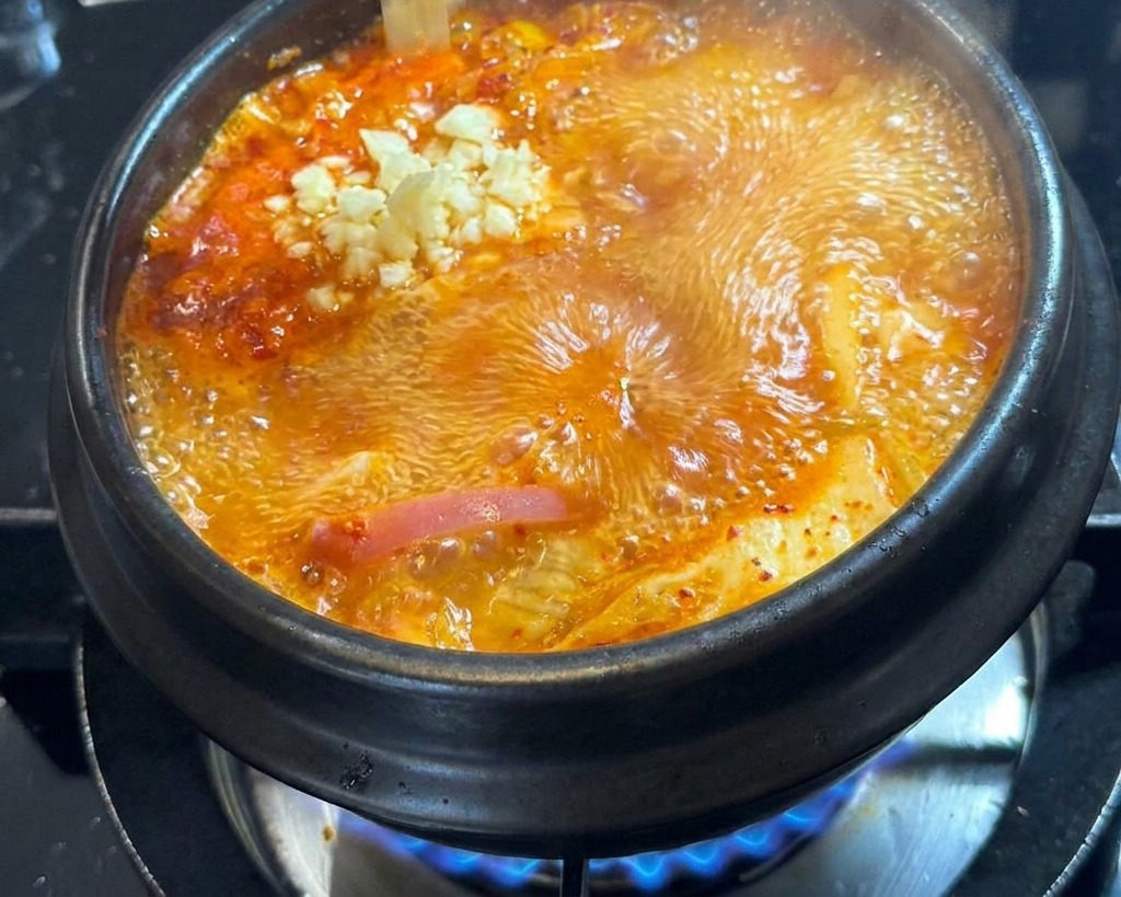 De lail frais haché déposé à la main au centre dun pot de soupe rouge en ébullition.