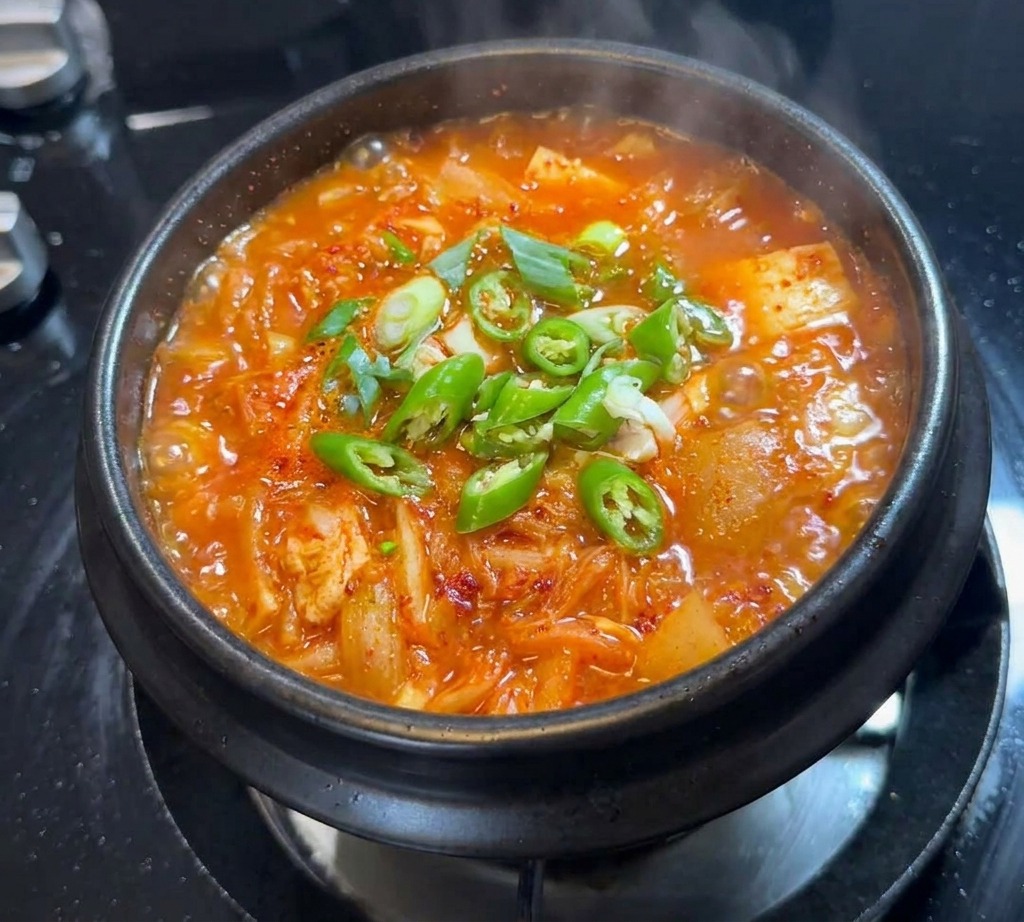 Rondelles de piment vert frais et quelques oignons verts parsemés à la surface dun ragoût de kimchi.