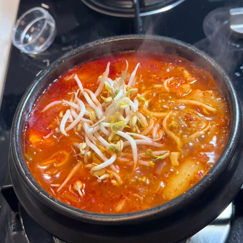 Un dôme de pousses de soja blanches et fraîches posé sur un pot noir de soupe de kimchi rouge.
