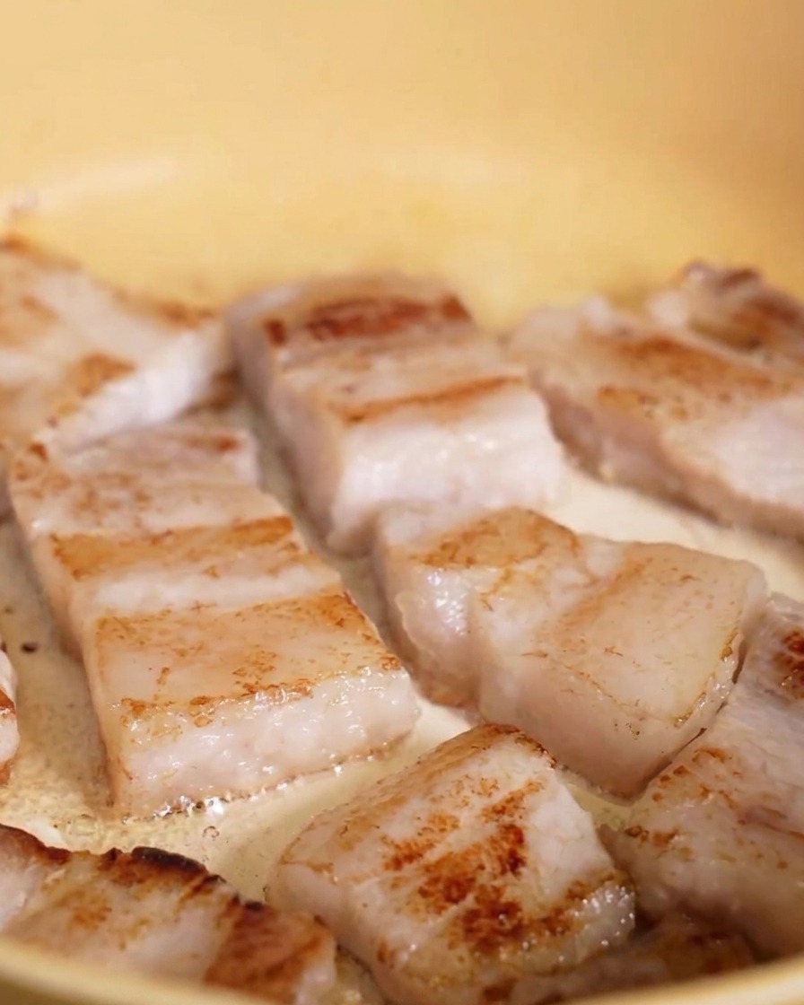 Tranches de poitrine de porc grillant dans une poêle jaune, montrant une croûte dorée appétissante.