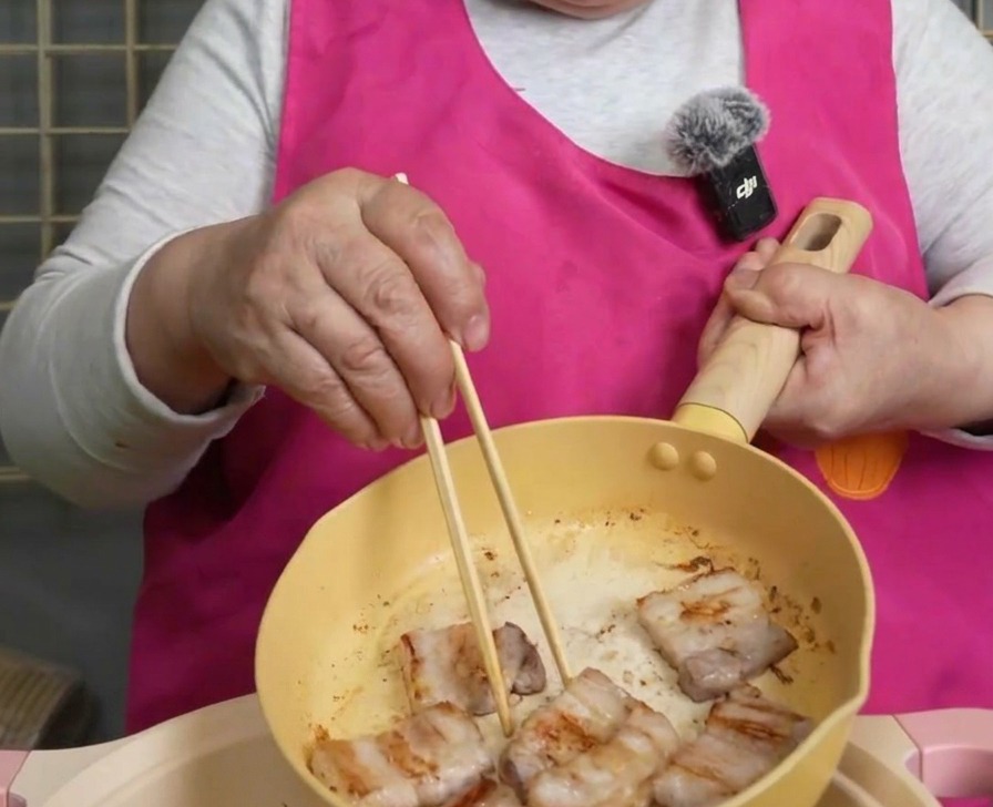 Tranches de poitrine de porc croustillantes saisies avec des baguettes en bois au-dessus dune poêle.
