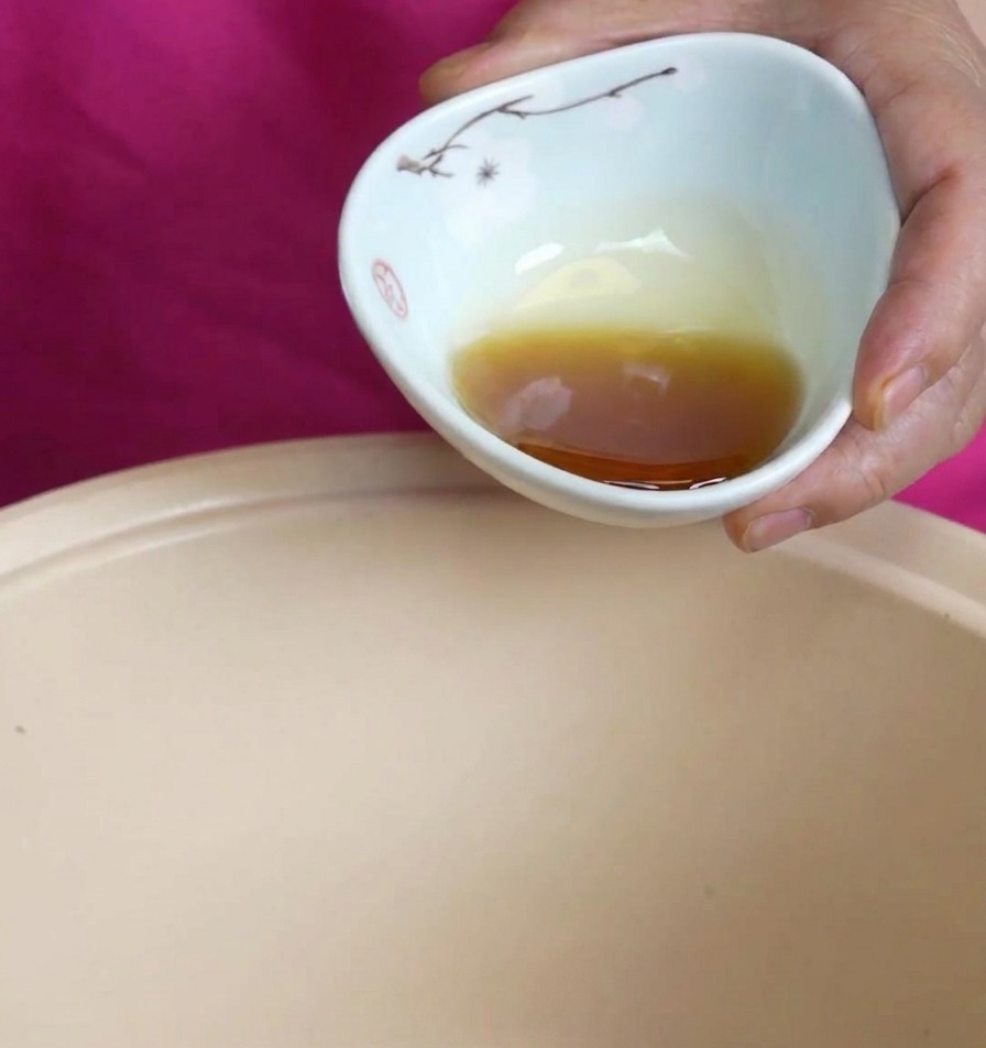 Huile de sésame ambrée versée dun petit bol en céramique dans une marmite de cuisson beige.
