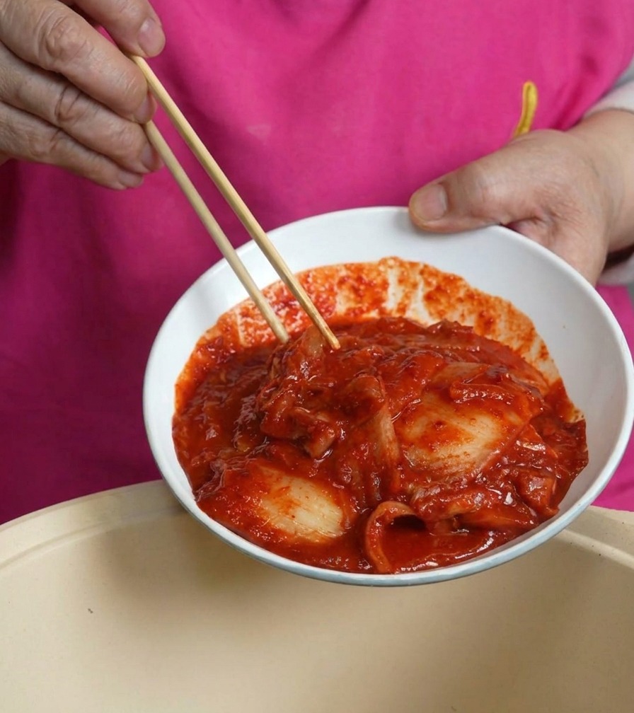Un bol blanc rempli de kimchi rouge et pimenté versé dans une marmite de cuisson.