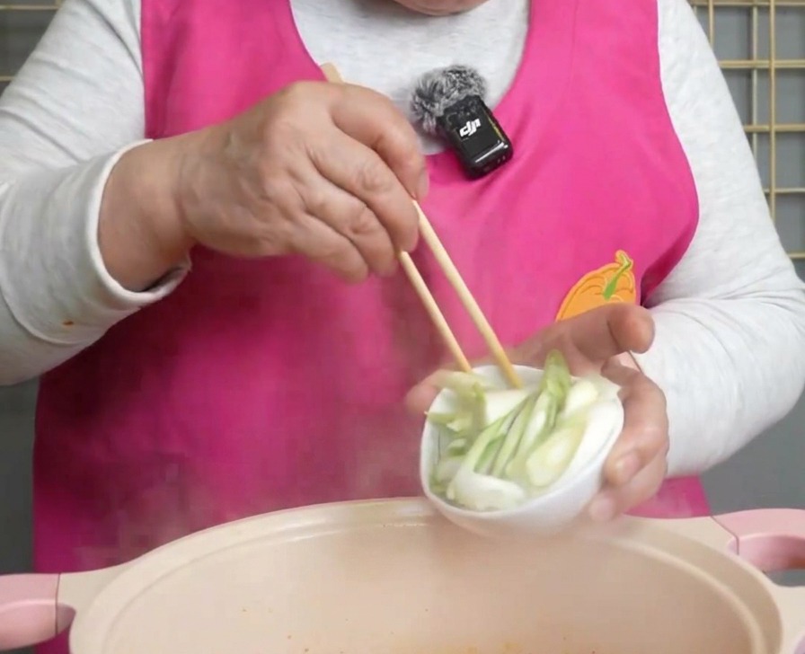 Oignons verts fraîchement hachés versés dun petit bol blanc dans la soupe de kimchi fumante.