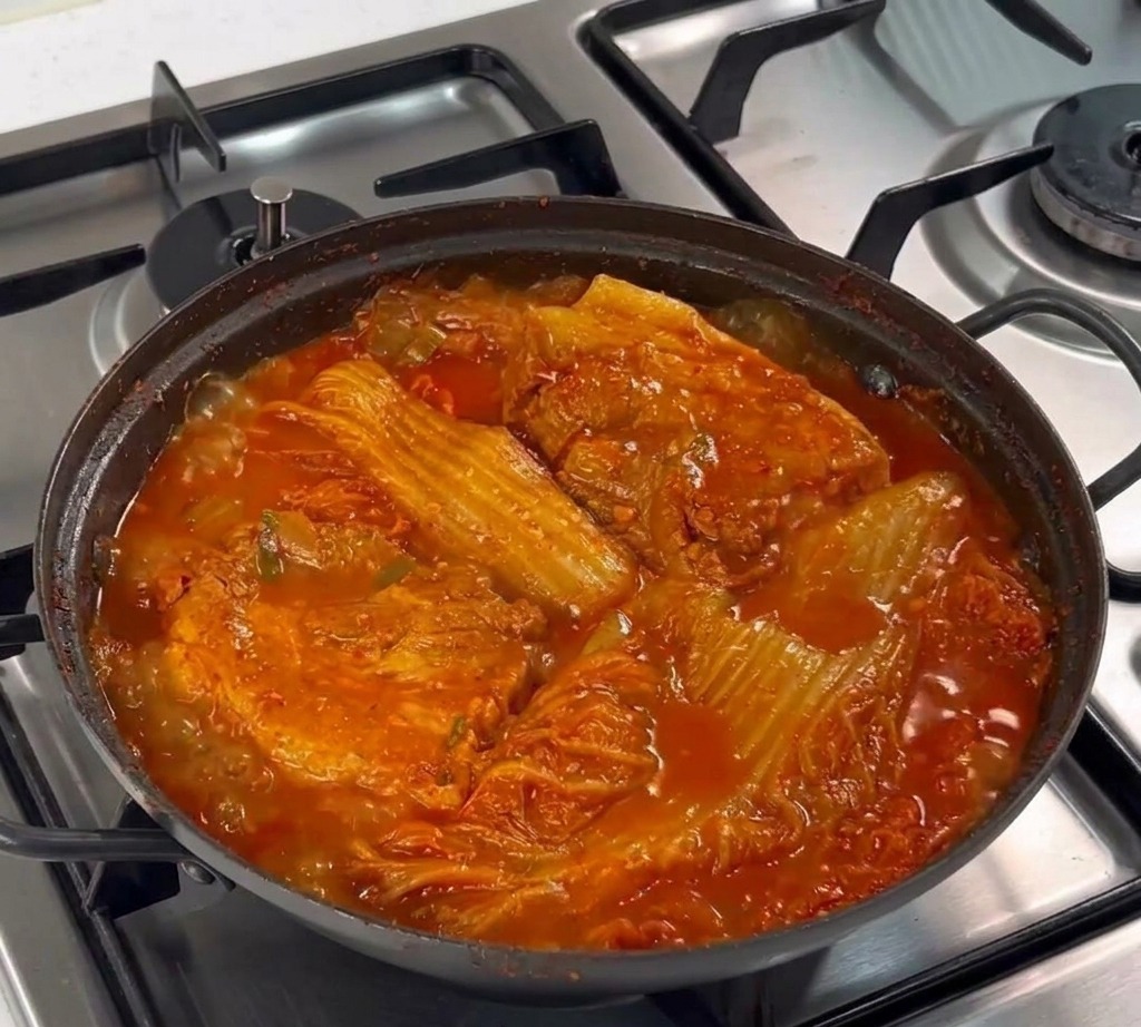 Une cuillère en métal déposant de lail haché sur la poitrine de porc crue dans la poêle.