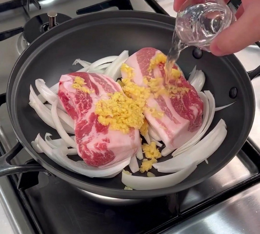 Un petit verre de vin de riz clair versé sur la poitrine de porc surmontée dail haché.