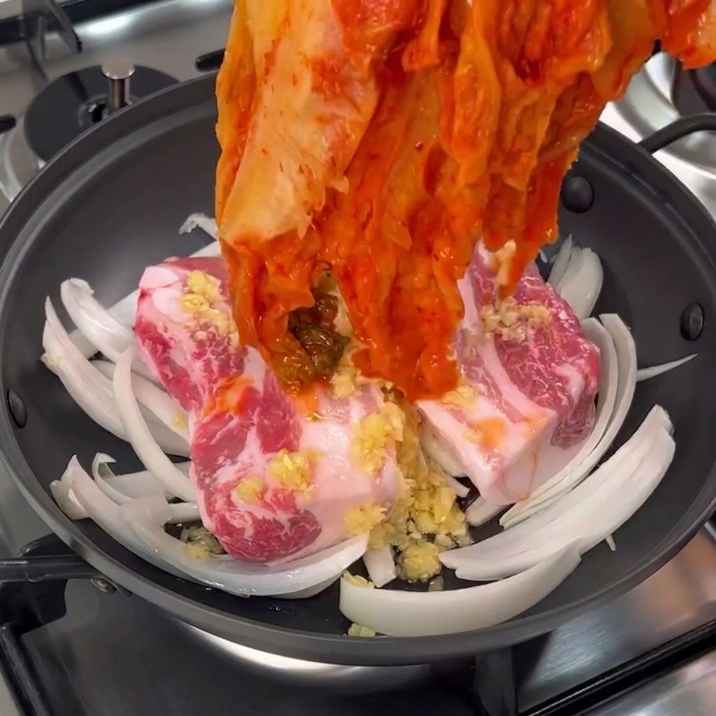 Une main plaçant un large bouquet de kimchi de chou fermenté rouge sur les morceaux de porc.