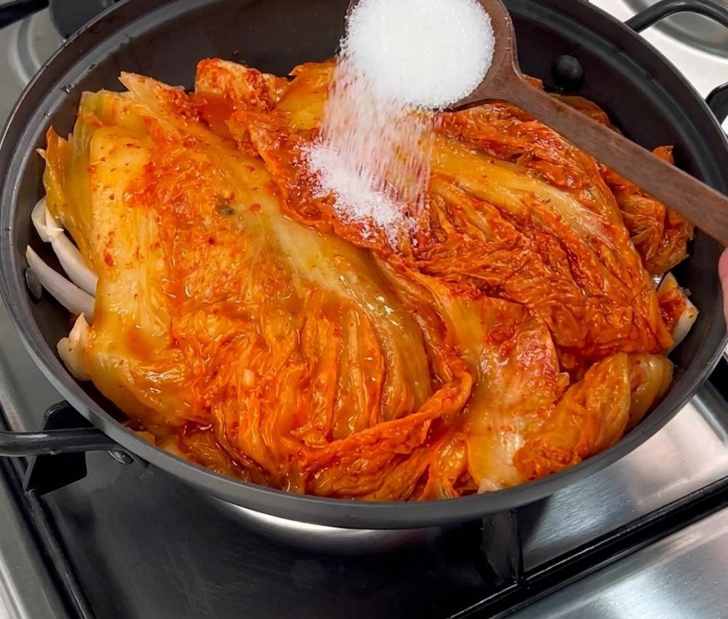 Du sucre blanc en poudre saupoudré avec une cuillère en bois sur le kimchi rouge.