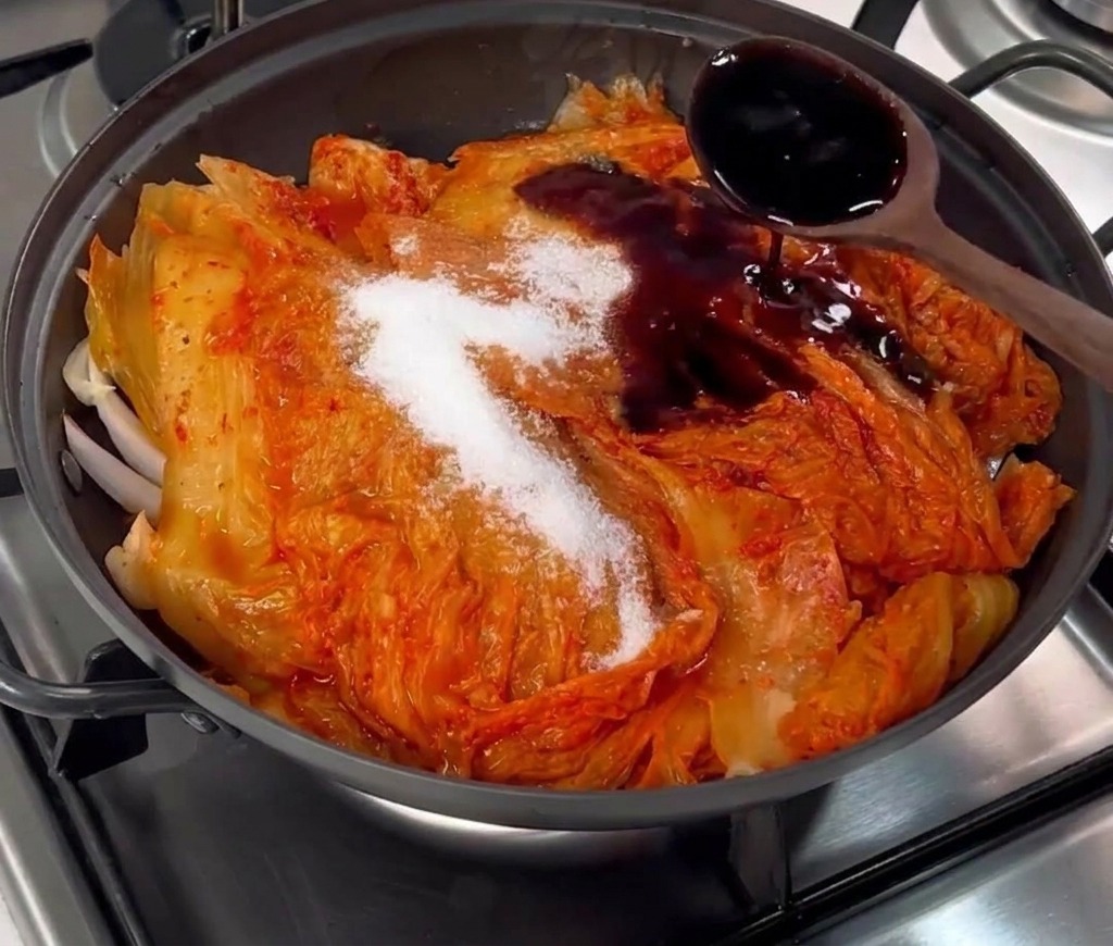 De la sauce soja brune versée avec une cuillère en bois sur le kimchi et le sucre.