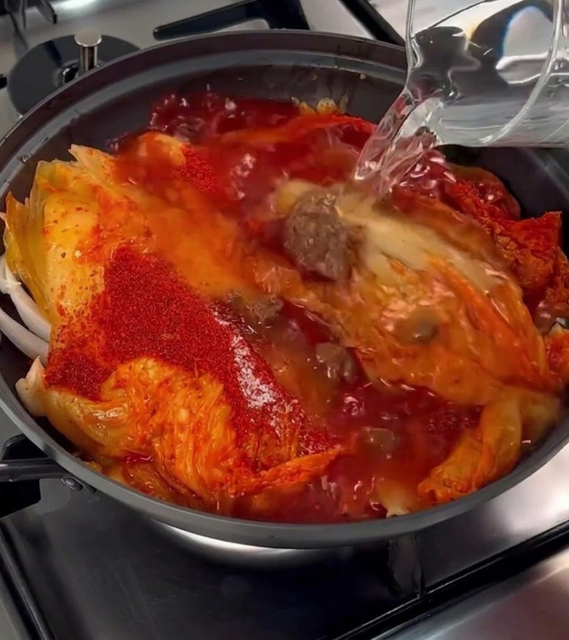 De leau claire versée depuis une carafe dans la poêle contenant le kimchi, le porc et le piment.