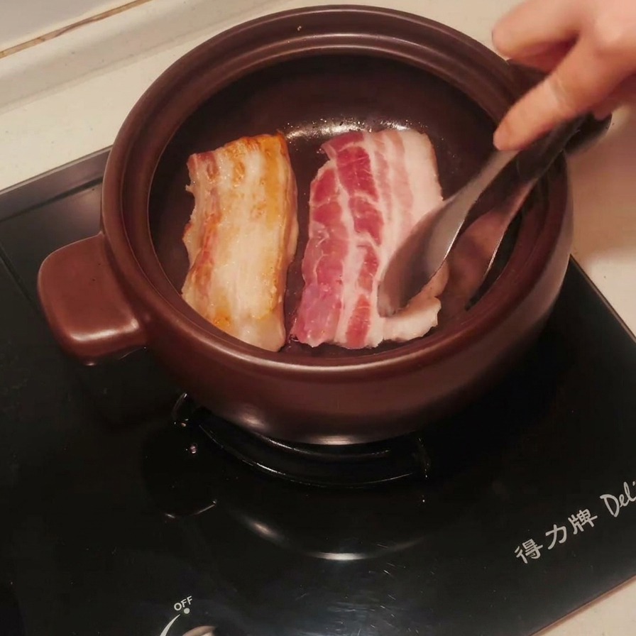 Tranches de poitrine de porc dans un pot en terre cuite, retournées pour montrer une face dorée.