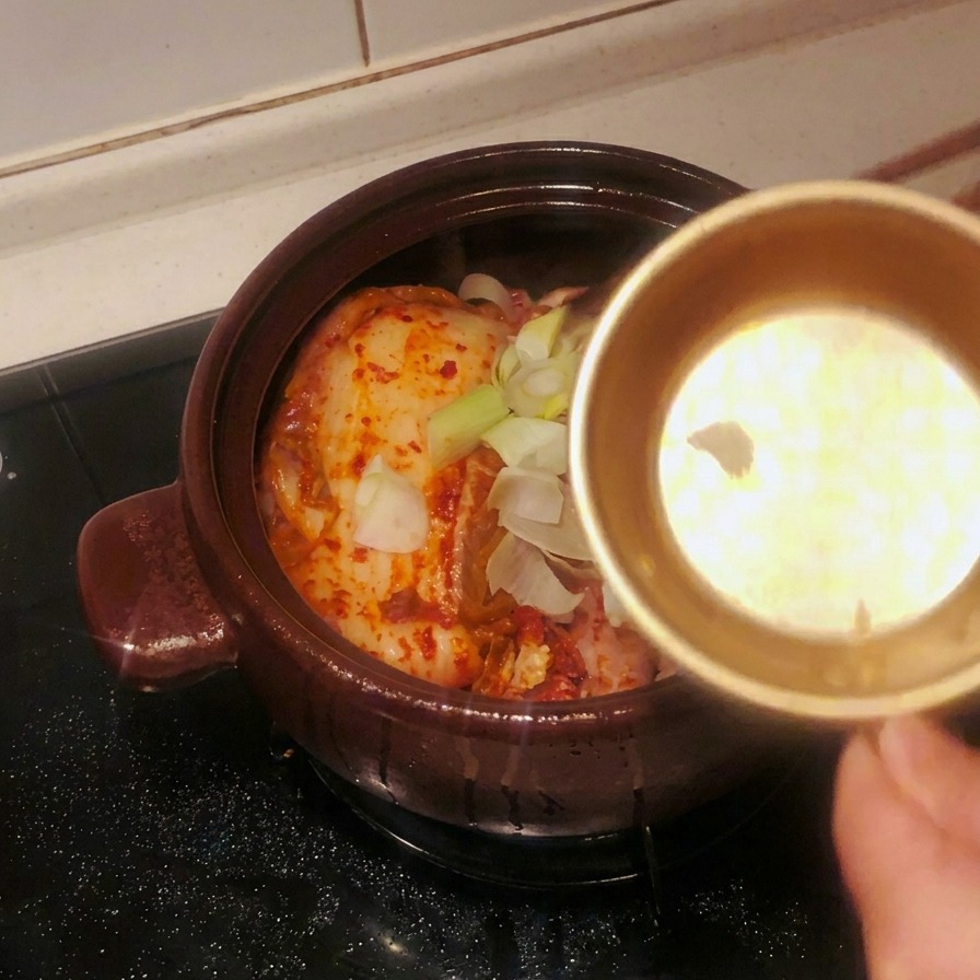 Bol en métal versant de lail émincé et de gros morceaux doignons verts sur le kimchi dans le pot.