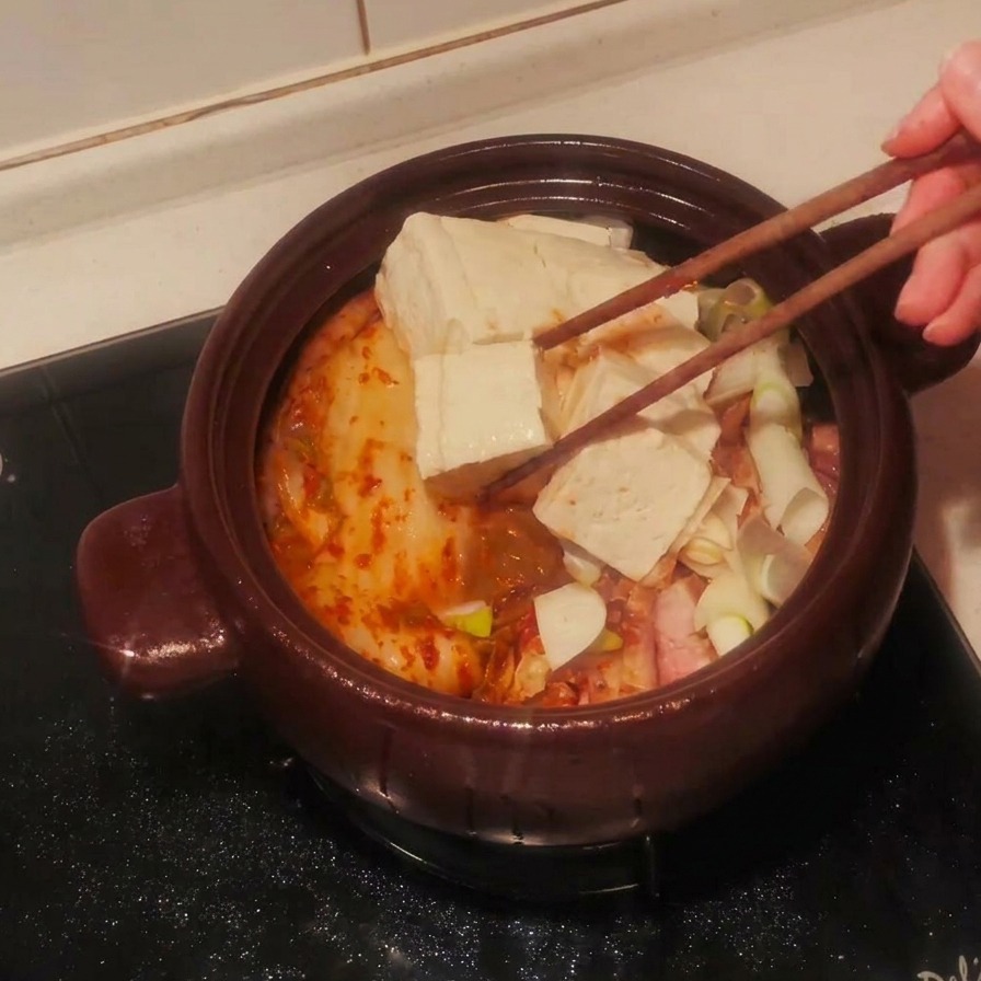 Tranches de tofu blanc disposées avec soin sur les ingrédients du ragoût dans le pot.