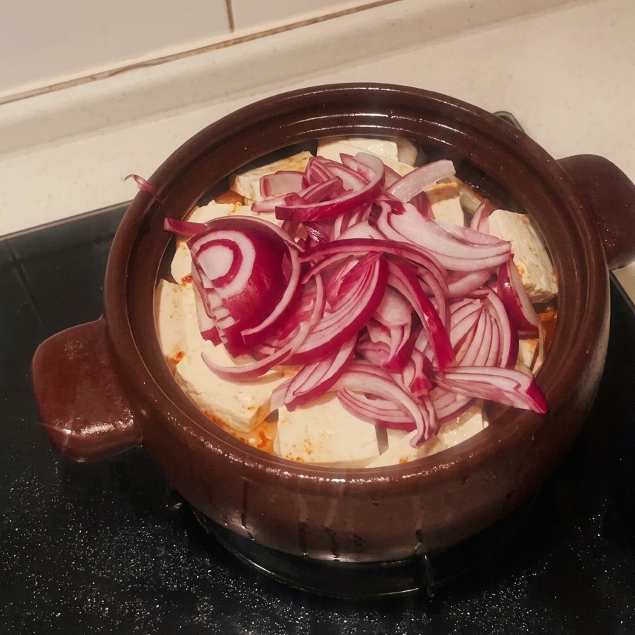 Une couche doignons rouges émincés recouvrant le tofu blanc dans le pot en terre cuite.
