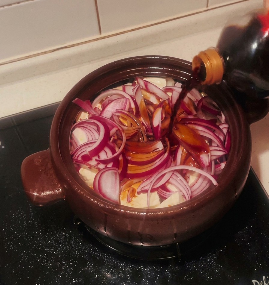 Sauce soja versée sur les oignons rouges et le tofu dans le pot en terre cuite.