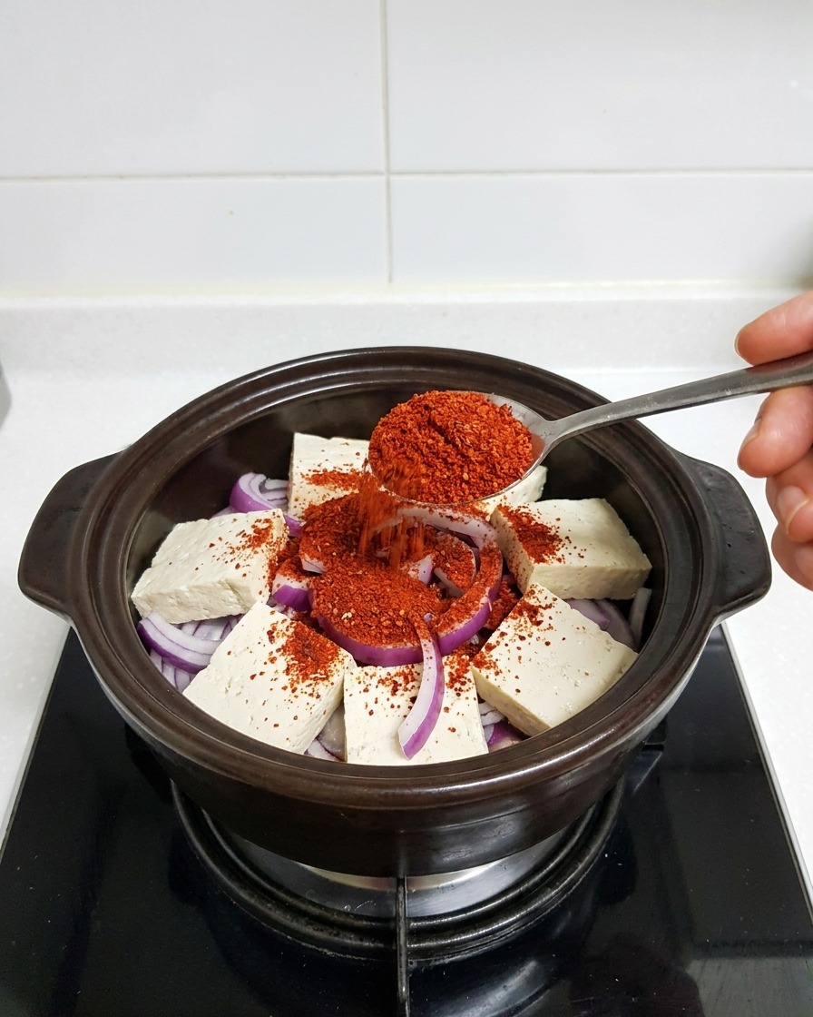Cuillère en métal déposant de la poudre de piment rouge vif sur le tofu et les oignons.