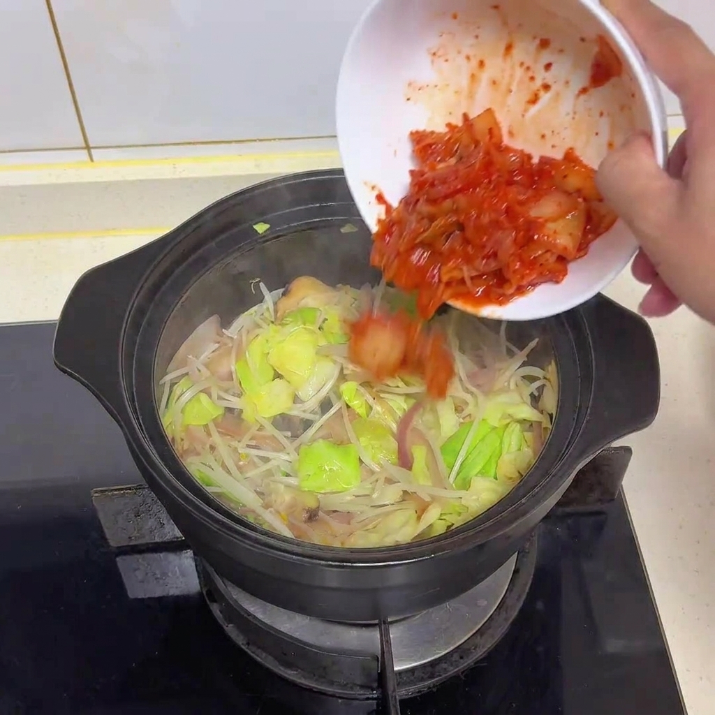 Kimchi rouge vif haché versé dun bol blanc dans une marmite de légumes sautés.