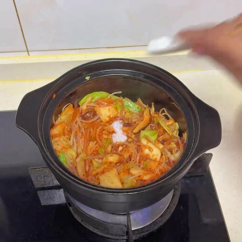 Une pincée de sel blanc ajoutée à la marmite de légumes et de kimchi sautés.