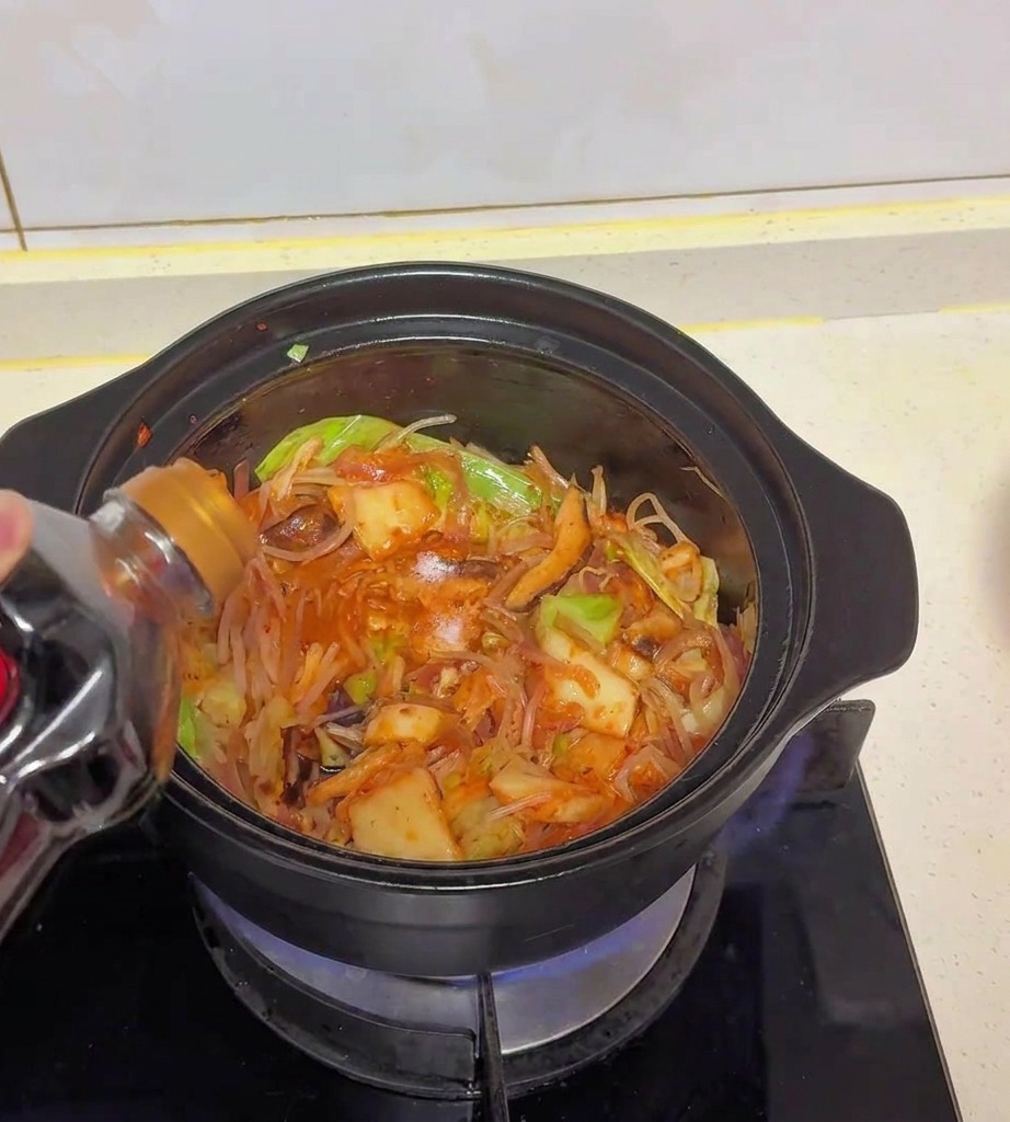Sauce soja claire versée dune bouteille en plastique sombre dans la marmite remplie de chou, kimchi et champignons.