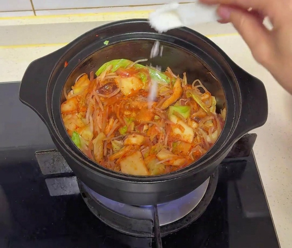 Une main utilisant une petite cuillère blanche pour saupoudrer du sucre sur les légumes en cuisson.