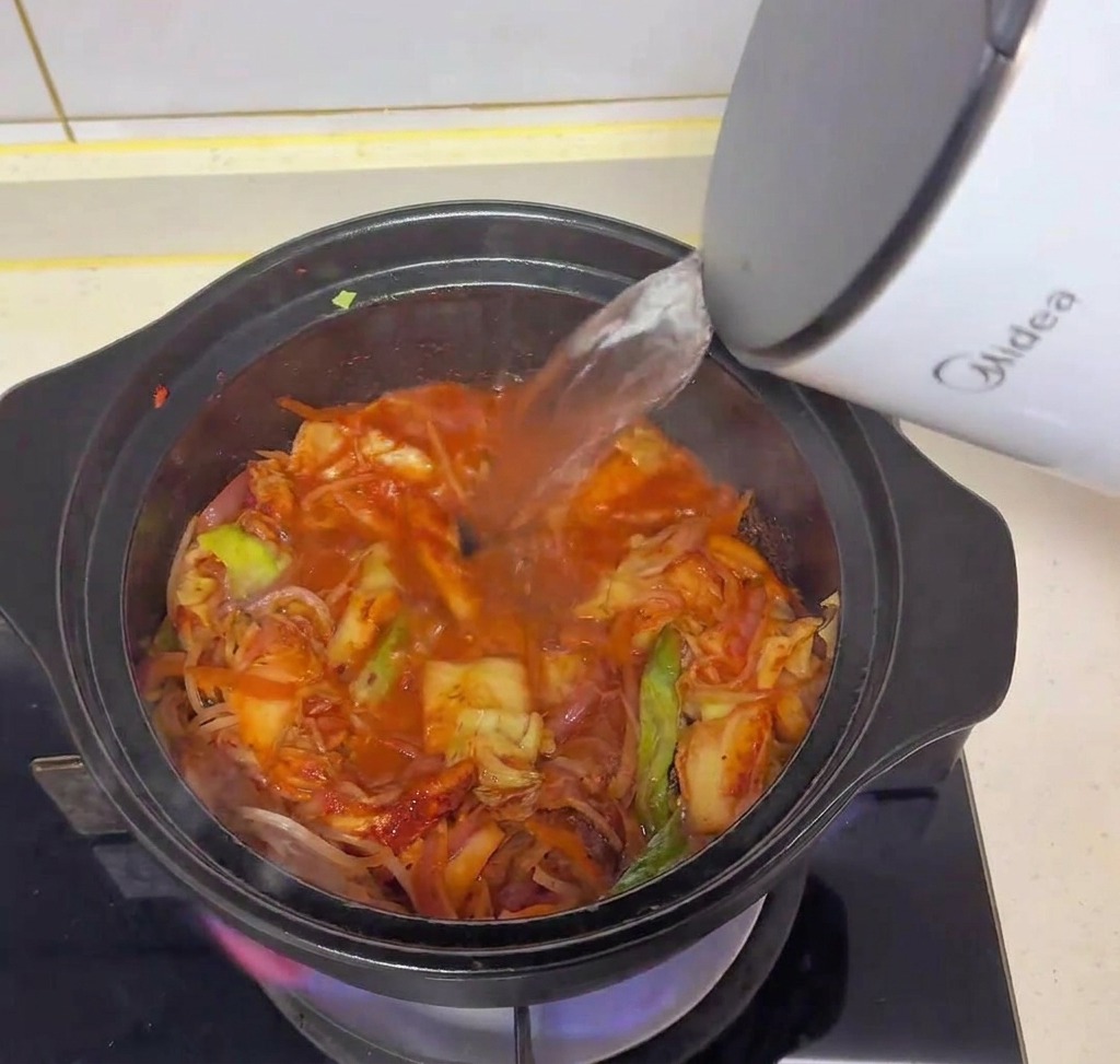 Eau chaude versée dune bouilloire électrique blanche dans la marmite de kimchi et légumes.