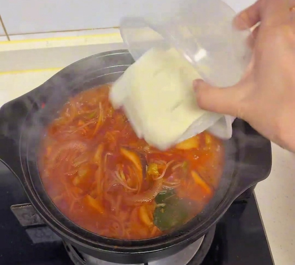 Cubes de tofu blanc frais versés dans une marmite de soupe au kimchi en ébullition.
