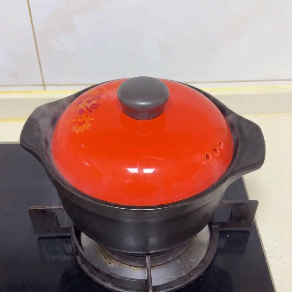 Un couvercle en céramique rouge couvrant la marmite sur une cuisinière à gaz avec de la vapeur séchappant.