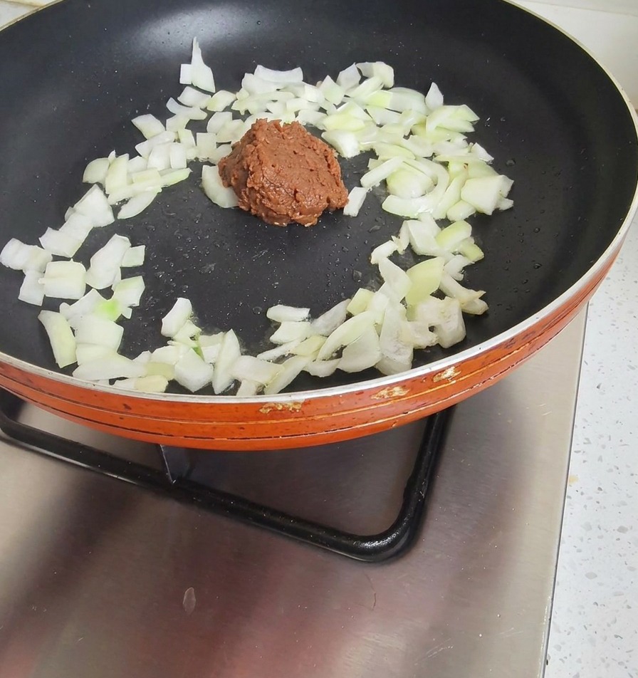 Une cuillerée de pâte de soja brun foncé ajoutée aux oignons revenus.