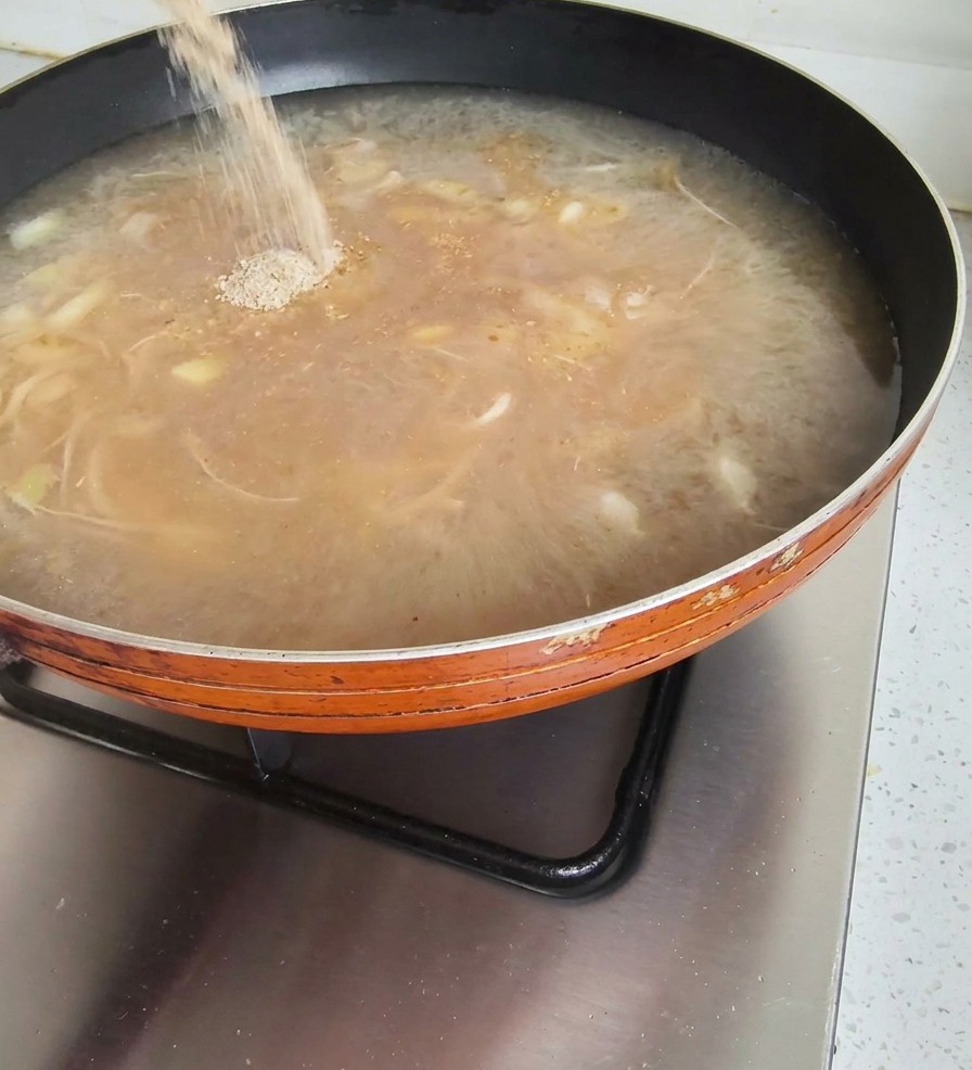 Poudre dassaisonnement versée dun sachet dans un bouillon brun bouillonnant sur le feu.