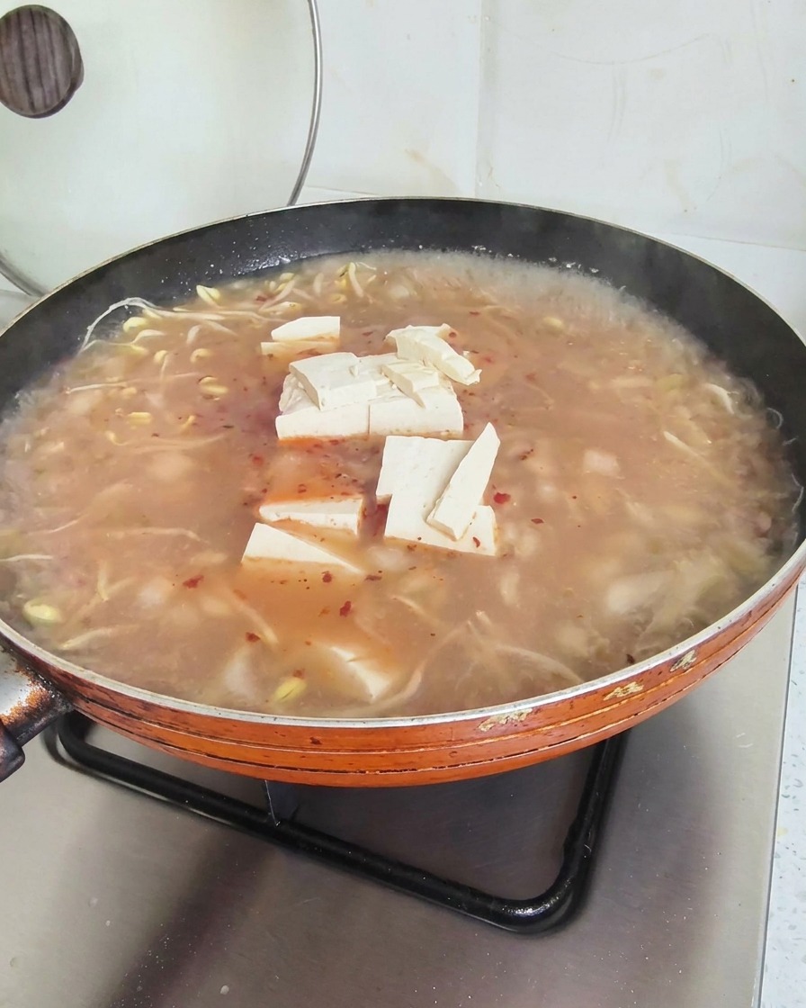 Cubes de tofu à la surface dune soupe rougeâtre frémissante dans une grande poêle orange.