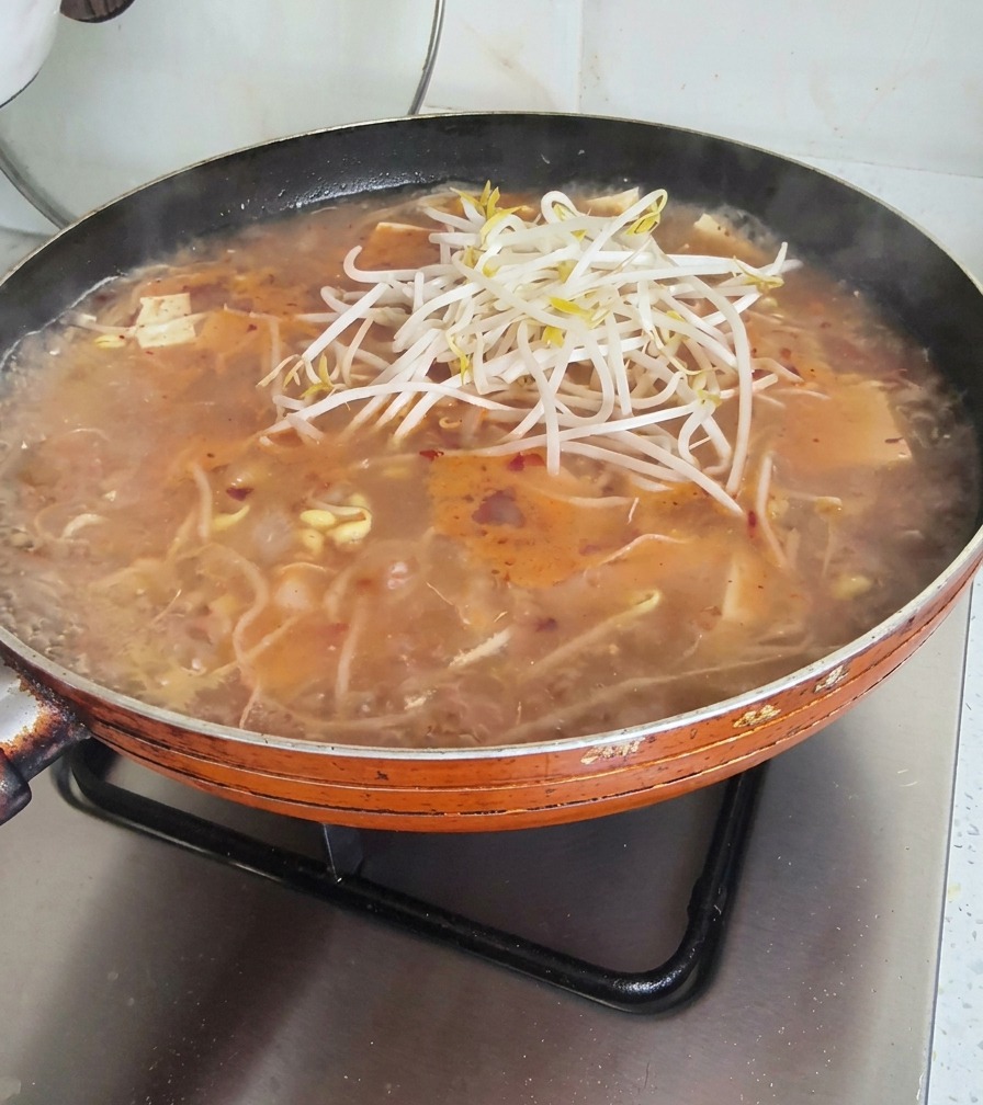 Pile de pousses de soja fraîches ajoutée sur une poêle de soupe bouillonnante.