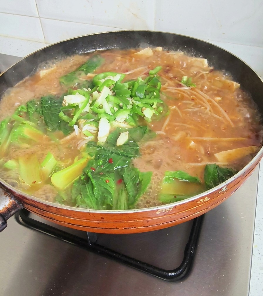 Poêle de soupe coréenne bouillonnante garnie de légumes verts, piments tranchés et ail haché.