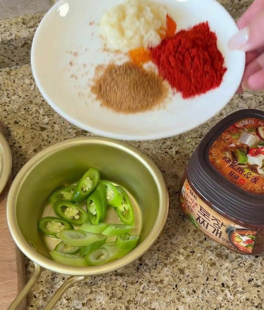 Une main tenant une assiette avec de lail et des épices à côté dun bol de piments et dun pot de pâte de soja.