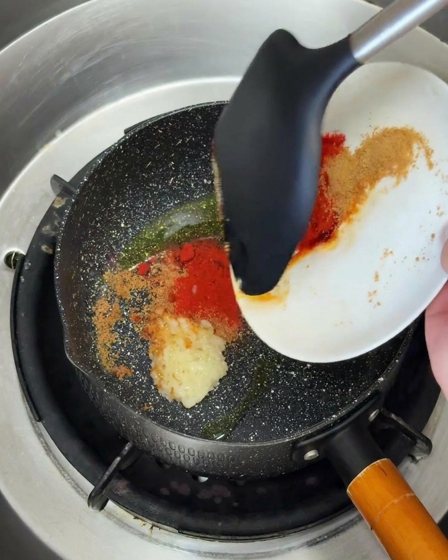 De lail haché et de la poudre de piment versés dans une poêle chaude avec de lhuile.