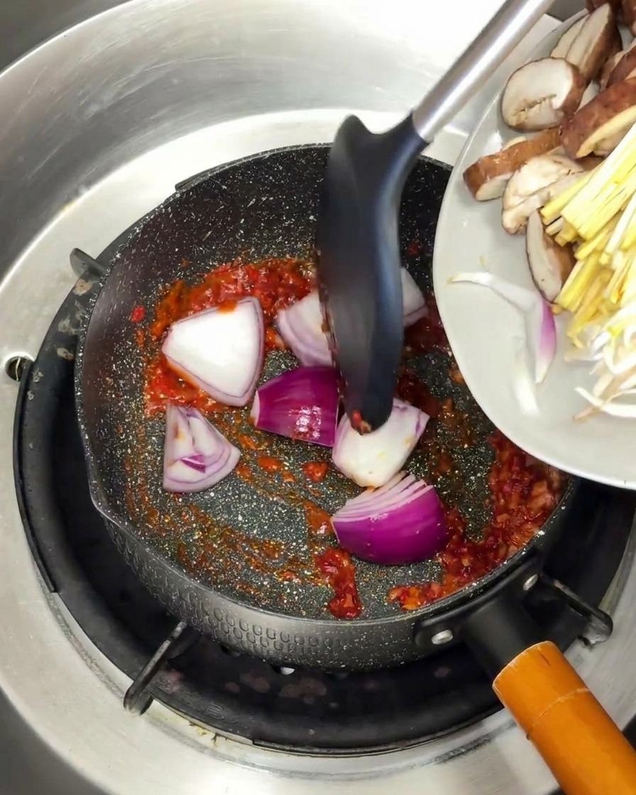 Des quartiers doignon rouge et des champignons ajoutés dans une poêle avec une base dépices rougeoyante.