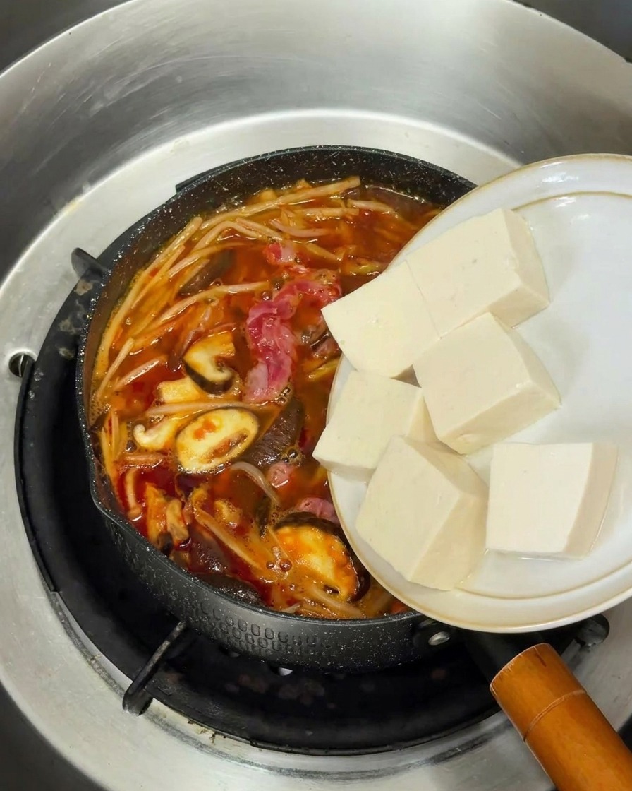 Cubes de tofu blanc frais ajoutés dans la soupe coréenne au bœuf en ébullition.