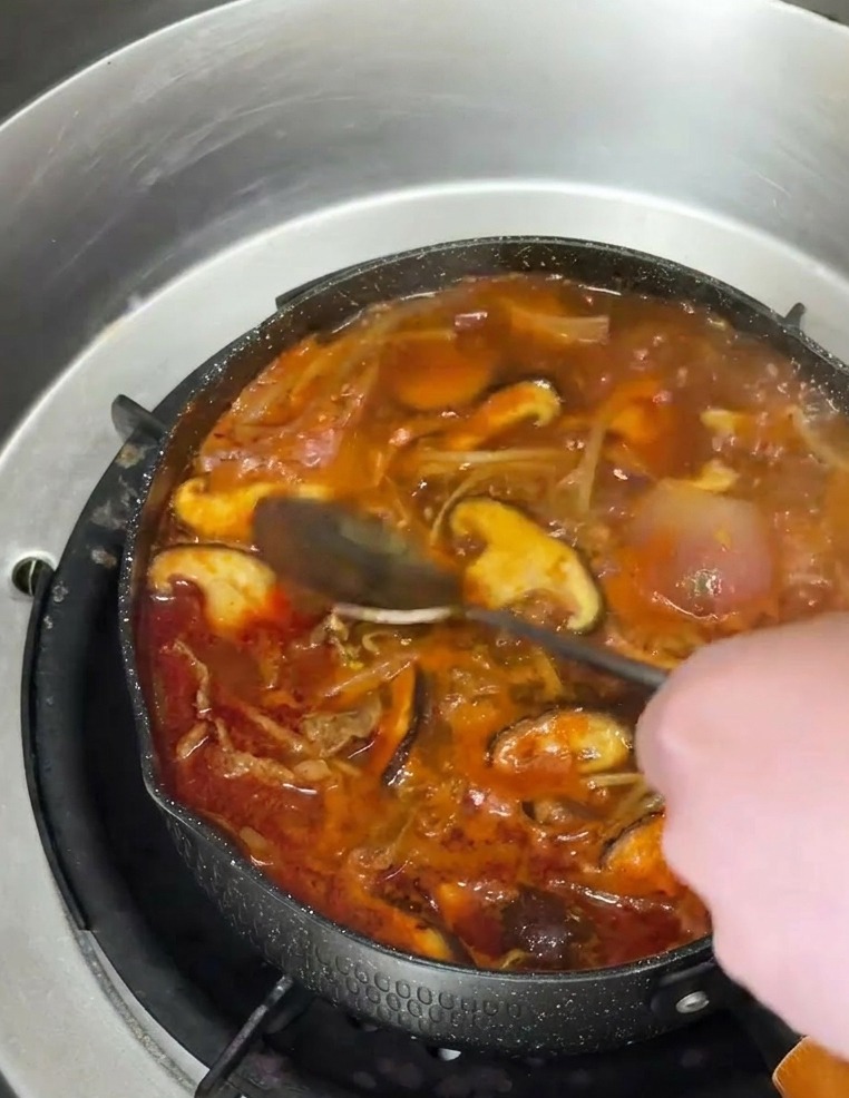 Une cuillère versant de lhuile de sésame ambrée dans une soupe épicée garnie de champignons.