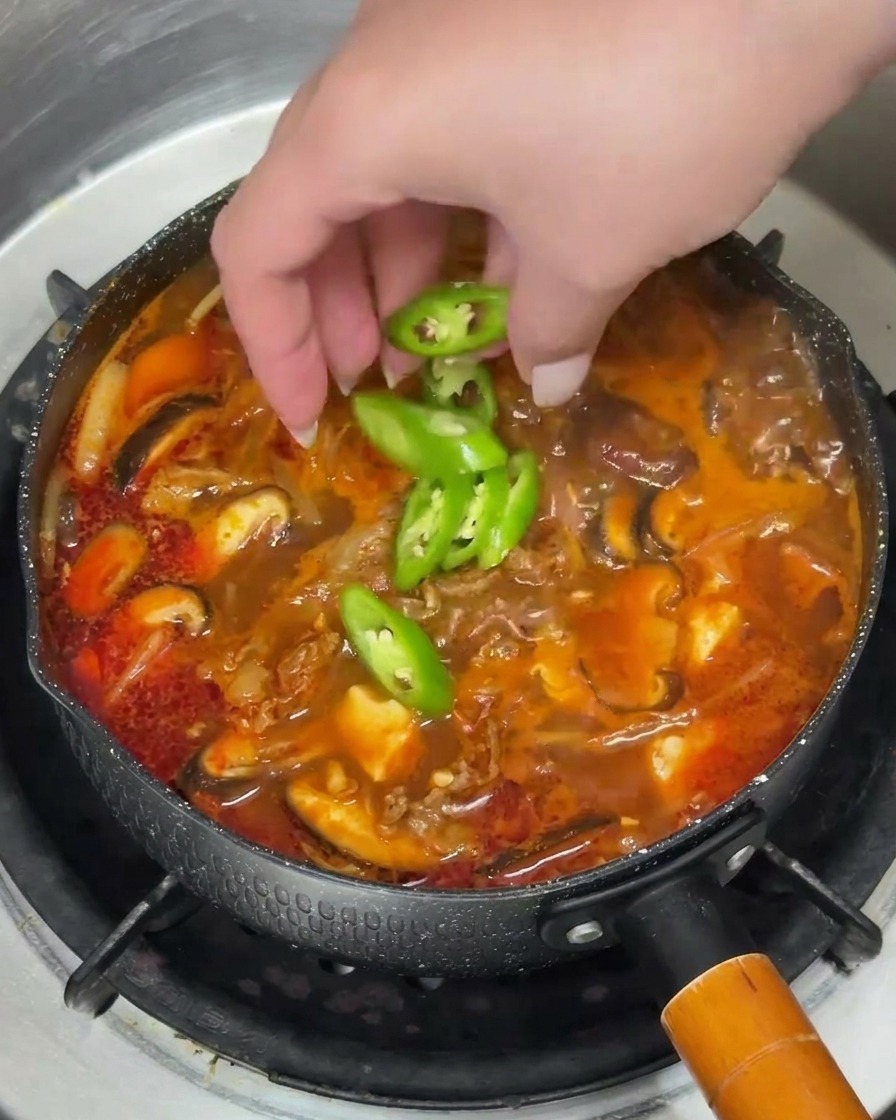 Une main parsemant des rondelles de piment vert et des oignons verts ciselés dans une soupe fumante.