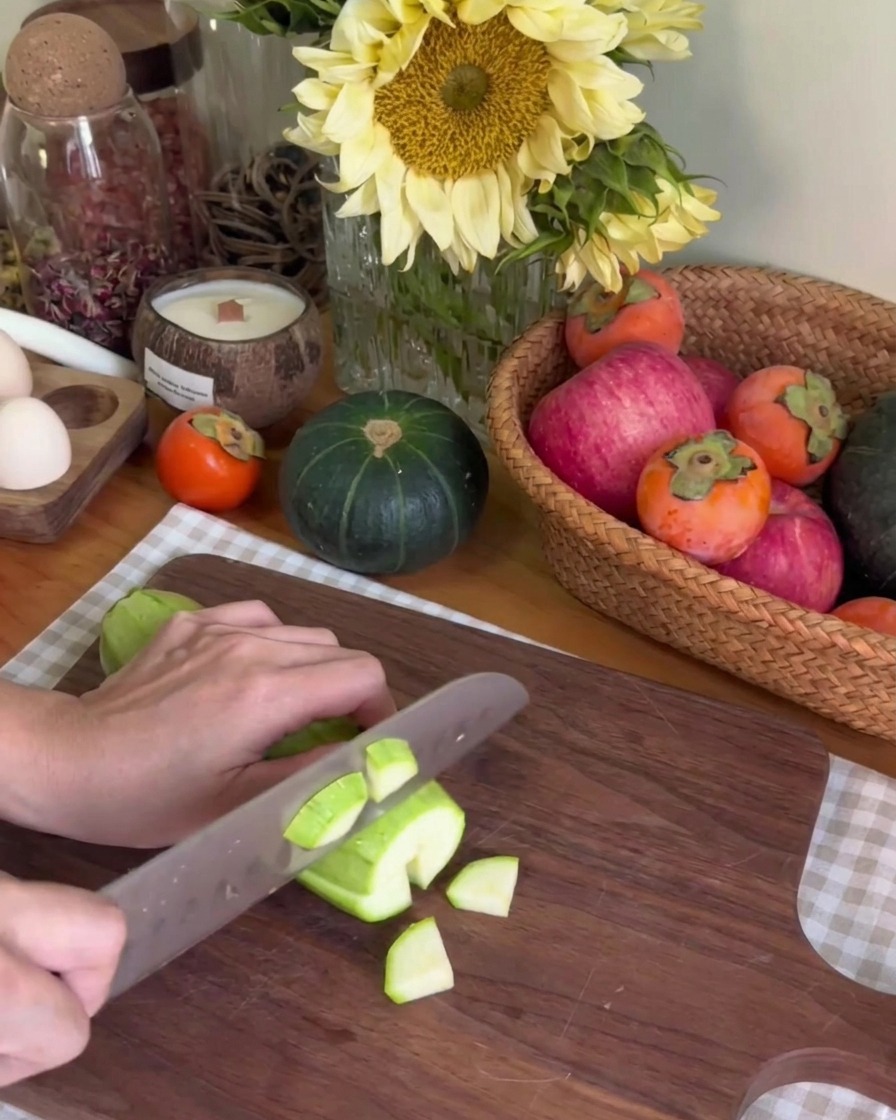 Une personne coupant une courgette verte en petits morceaux sur une planche en bois sombre
