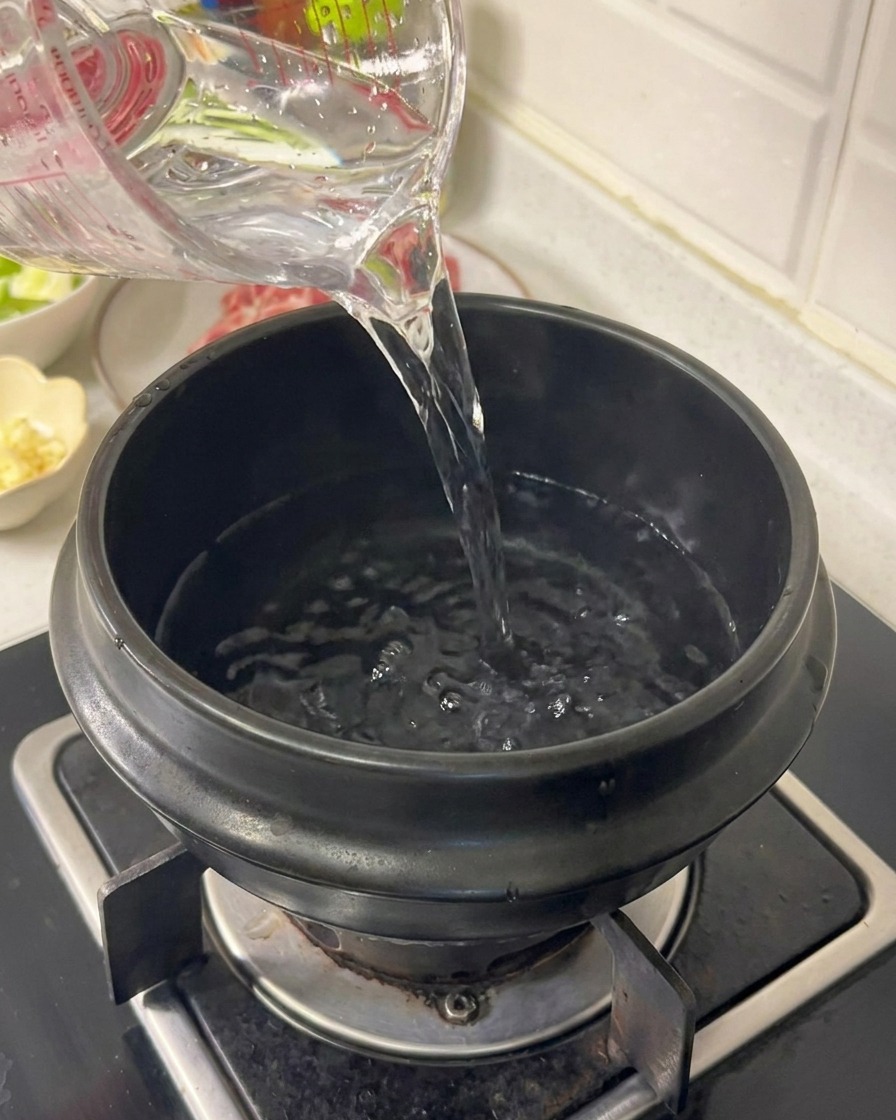 Versement deau depuis un verre doseur dans une marmite en céramique noire sur une cuisinière à gaz