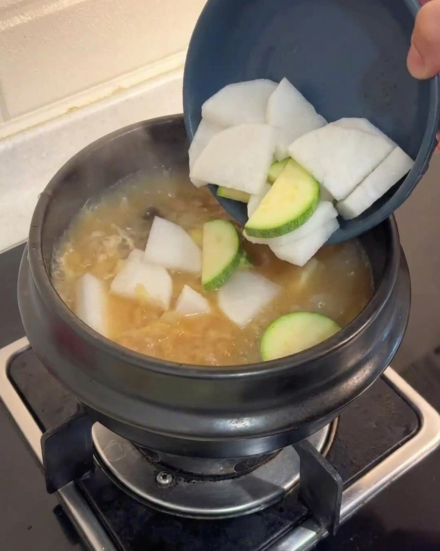 Slices de radis blanc et de courgette versées dun bol bleu dans un bouillon brun bouillonnant