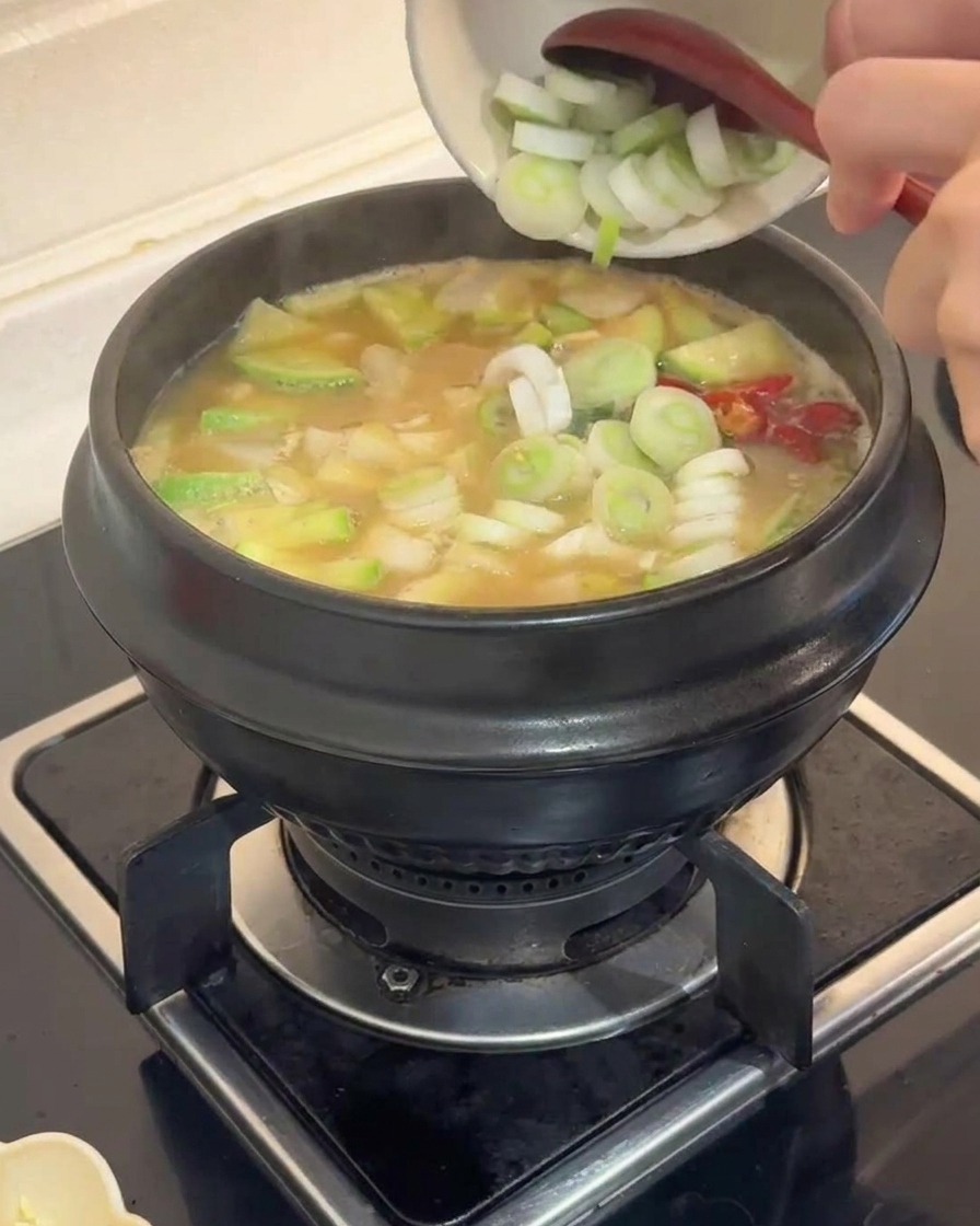 Rondelles de poireaux verts ajoutées dun petit bol blanc dans un ragoût de légumes bouillonnant
