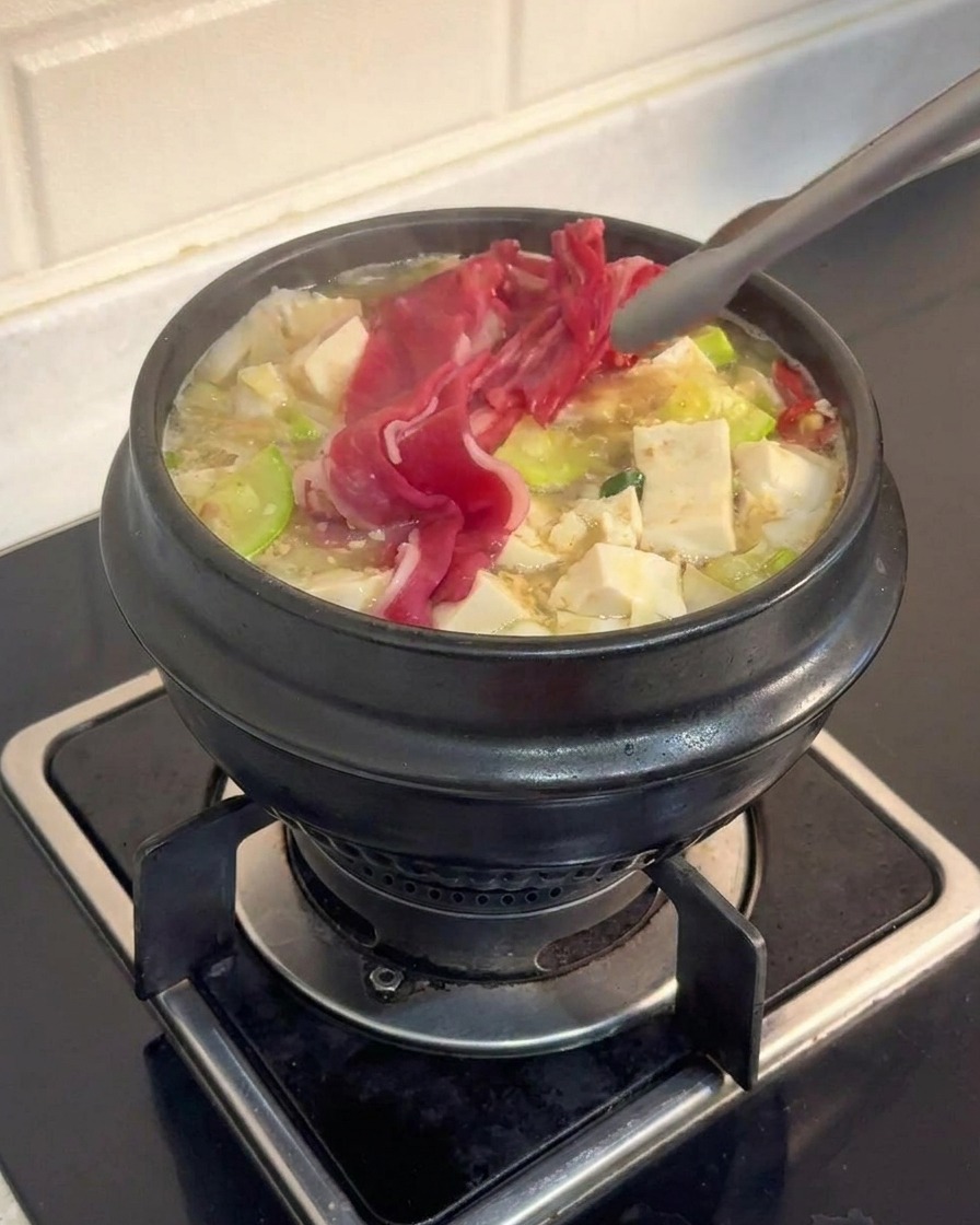 Pinces métalliques plaçant de fines tranches de bœuf cru marbré dans un ragoût bouillonnant avec du tofu et des légumes