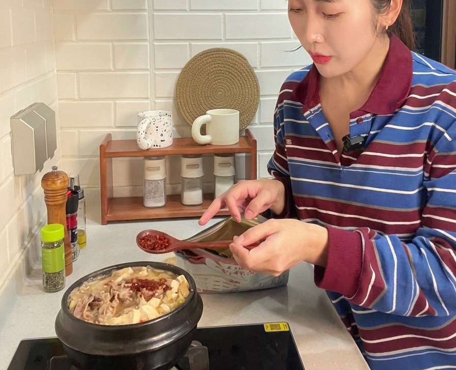 Cuillère en bois ajoutant de la poudre de piment rouge vif à un ragoût coréen bouillonnant avec du bœuf et du tofu